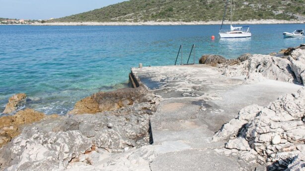 A rocky shoreline with clear blue water, a small pier, and boats in the distance. - One-Bedroom Apartment With Sea View Ap 2 (Sevid)