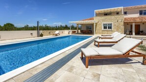 A modern pool area with lounge chairs, a stone building, and a clear blue sky. - Rustic Villa Perosa With Heated Pool (Zaton)