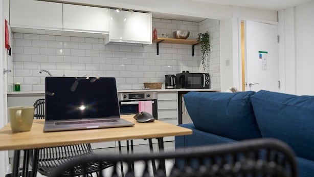 Una cocina moderna con baldosas blancas, un microondas, un hervidor y un ordenador portátil sobre una mesa.