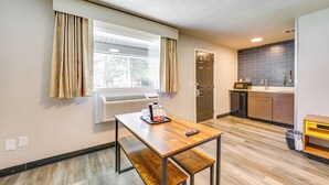 Eine kompakte Küche mit Einbauherd, Spüle und Mikrowelle. Ein Fenster mit Vorhängen, eine Sitzbank und ein Tisch mit Fernbedienung.