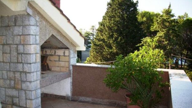 A stone-built outdoor kitchen area with a built-in grill, potted plants, and a tiled floor. - Two-Bedroom Apartment With Sea View (Malinska)