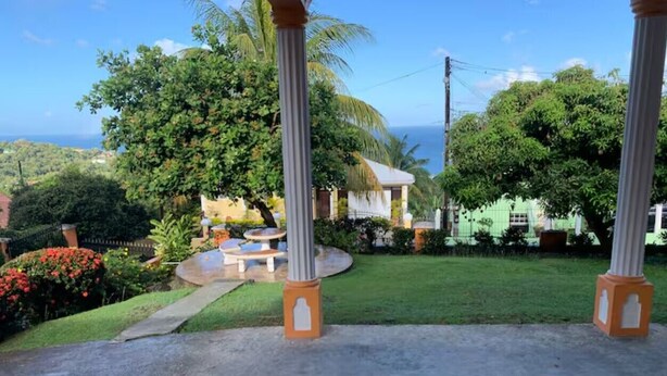 A courtyard with a concrete path, palm trees, and a small seating area with a table and chairs. - Anne Marie Villas - Ron (Castries)
