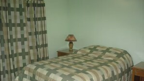 A bedroom with a bed, a nightstand, a lamp, and a curtain. - Anne Marie Villas - Ron (Castries)