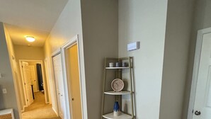 A hallway with a carpeted floor, a metal shelf unit with decorative items, and a patterned rug.