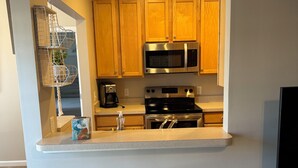 A compact kitchen with wooden cabinets, a microwave, a stove, and two bar stools.