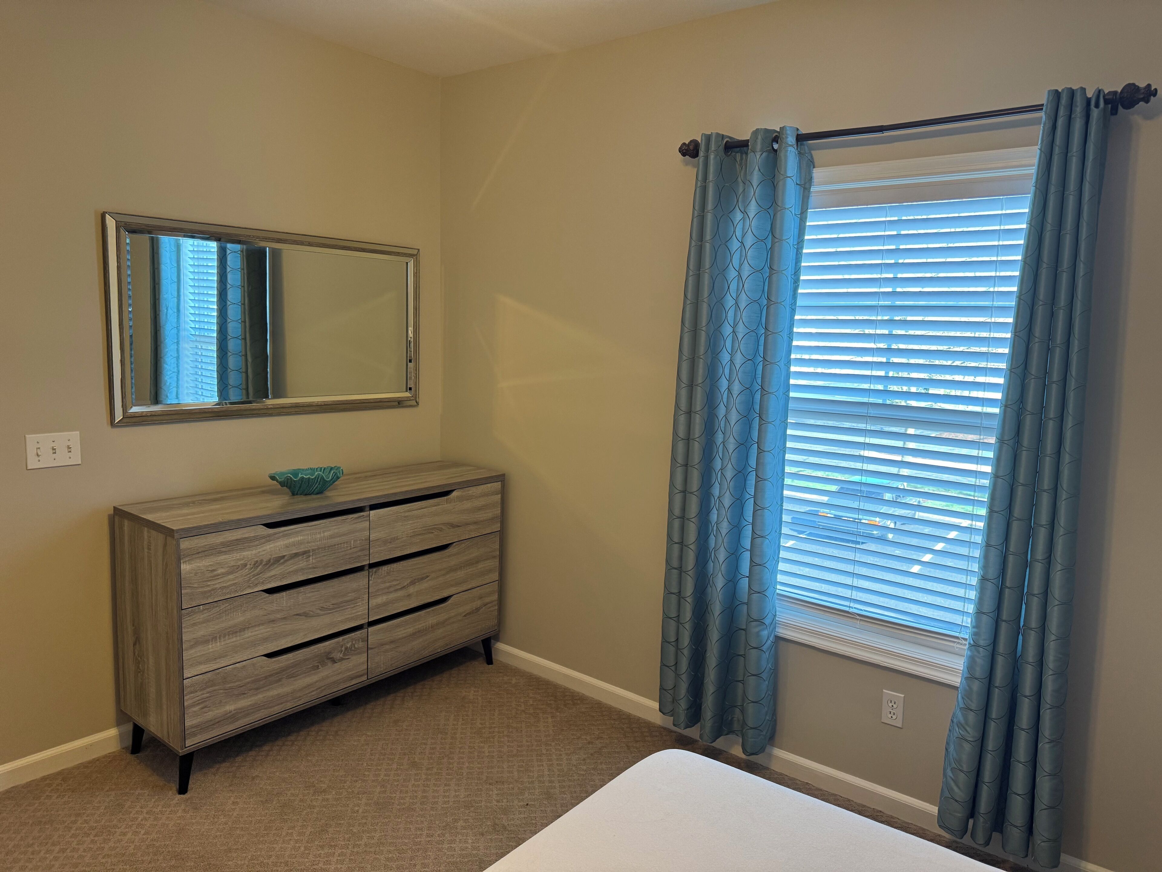 A bedroom with a wooden dresser, a mirror, and a window with blue curtains.