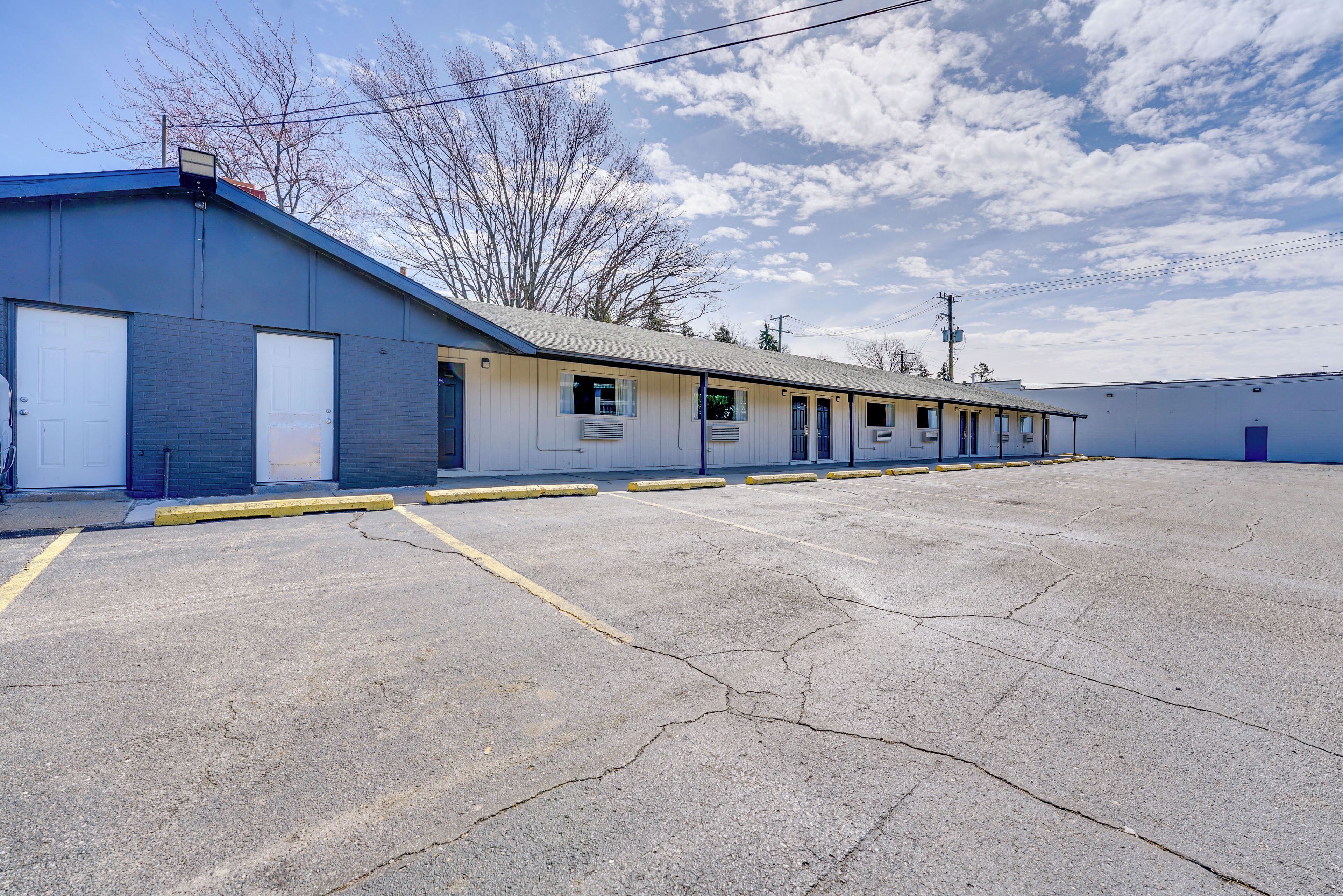 Un edificio industrial amplio con varias puertas de garaje, un estacionamiento y un cielo despejado.