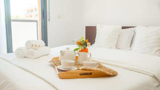 Un lit bien fait, avec du linge de lit blanc, un plateau avec un service à thé et un vase rempli de fleurs.