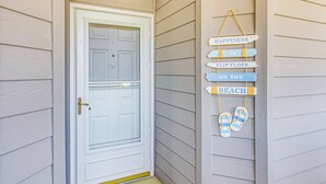 Eine weiße Tür mit Glasscheibe, eine Holzverkleidung mit horizontalen Brettern und ein Schild mit der Aufschrift "HAPPINESS IS FLIP FLOPS ON THE BEACH" an der Wand.