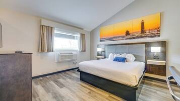 Een moderne hotelkamer met een groot bed, een bureau, een raam met gordijnen, een aan de muur bevestigd kunstwerk van een vuurtoren en een ingebouwde nachtkastje.