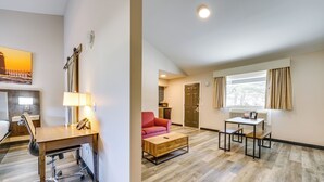 Ein modernes Hotelzimmer mit einem Holzbüro, einem roten Sofa, einem Couchtisch aus Holz und einem Esstisch mit Stühlen.