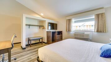 Ein Hotelzimmer mit Bett, Schreibtisch, Stuhl, Fernseher, Kleiderschrank und einem Fenster mit Vorhängen.