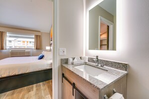 A hotel room with a bed, a bathroom with a sink and mirror, and a window with curtains. - Pet-Friendly Studio Near Lighthouse Beach! (Port Huron)