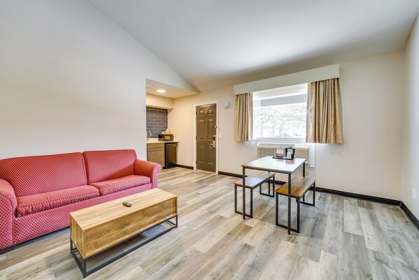 A compact living space with a red sofa, a wooden coffee table, a small dining table with benches, and a kitchen area in the background. - Pet-Friendly Studio Near Lighthouse Beach! (Port Huron)