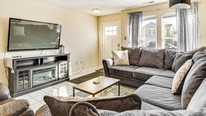 A living room with a large flat-screen TV, a dark-colored sofa, a wooden coffee table, and a fireplace. - 5 Mi to Eagle Creek Park: Home w/ Fenced Yard! (Indianapolis)