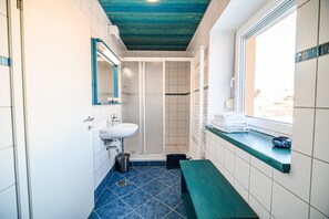A bathroom with a sink, mirror, shower, and a window with towels on the windowsill. - One Bedroom Apartment with Breakfast in Ančkin kot (Cerknica)