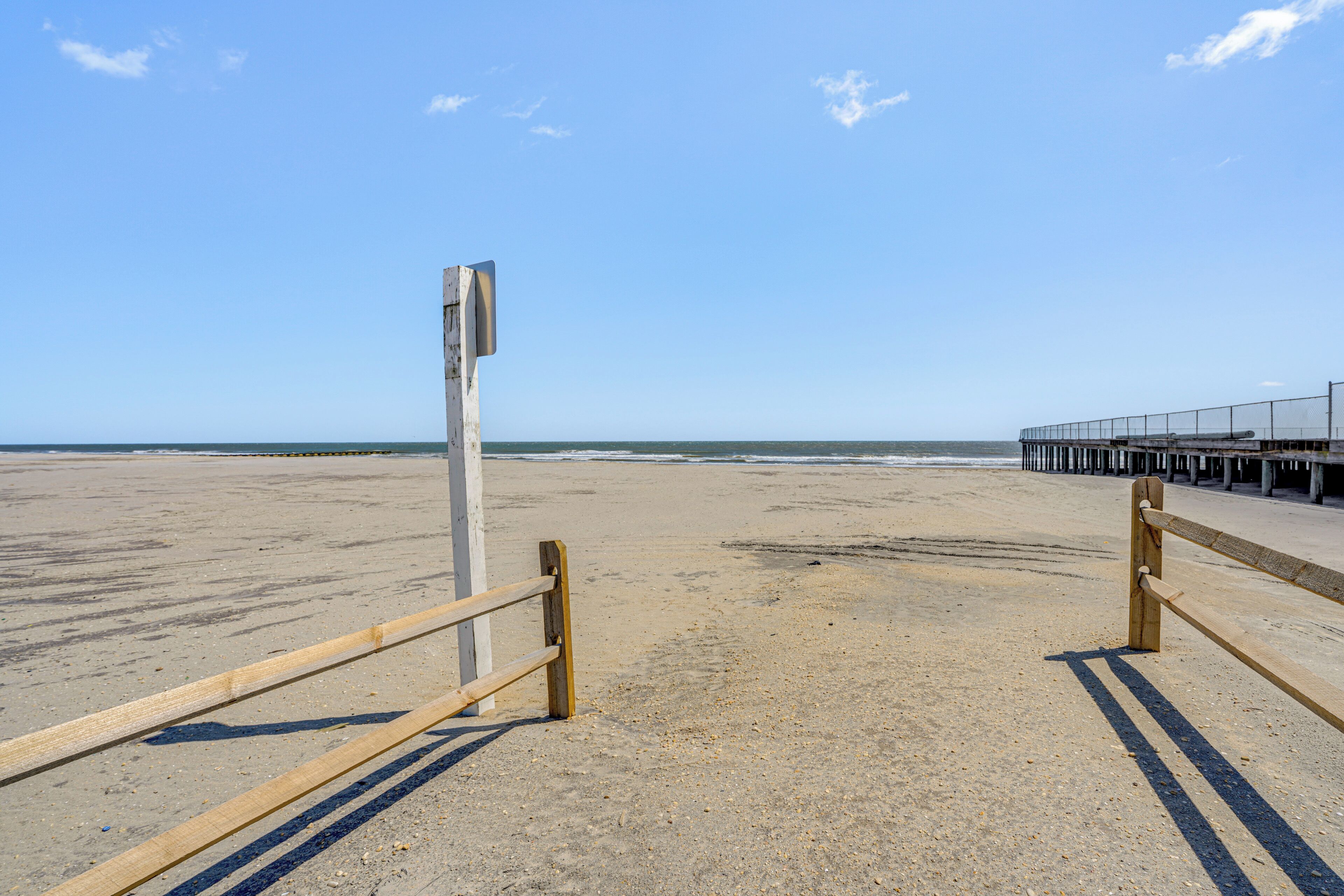 A beach with a wooden fence and a pier in the background.
