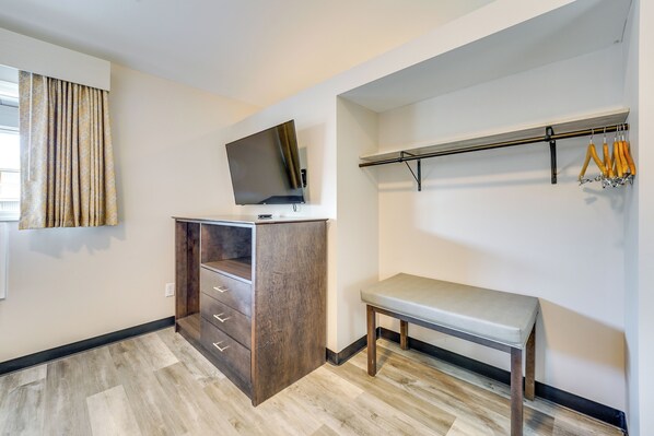 Une pièce comprenant un bureau en bois, un téléviseur fixé au mur, un banc et un porte-manteau avec des cintres.