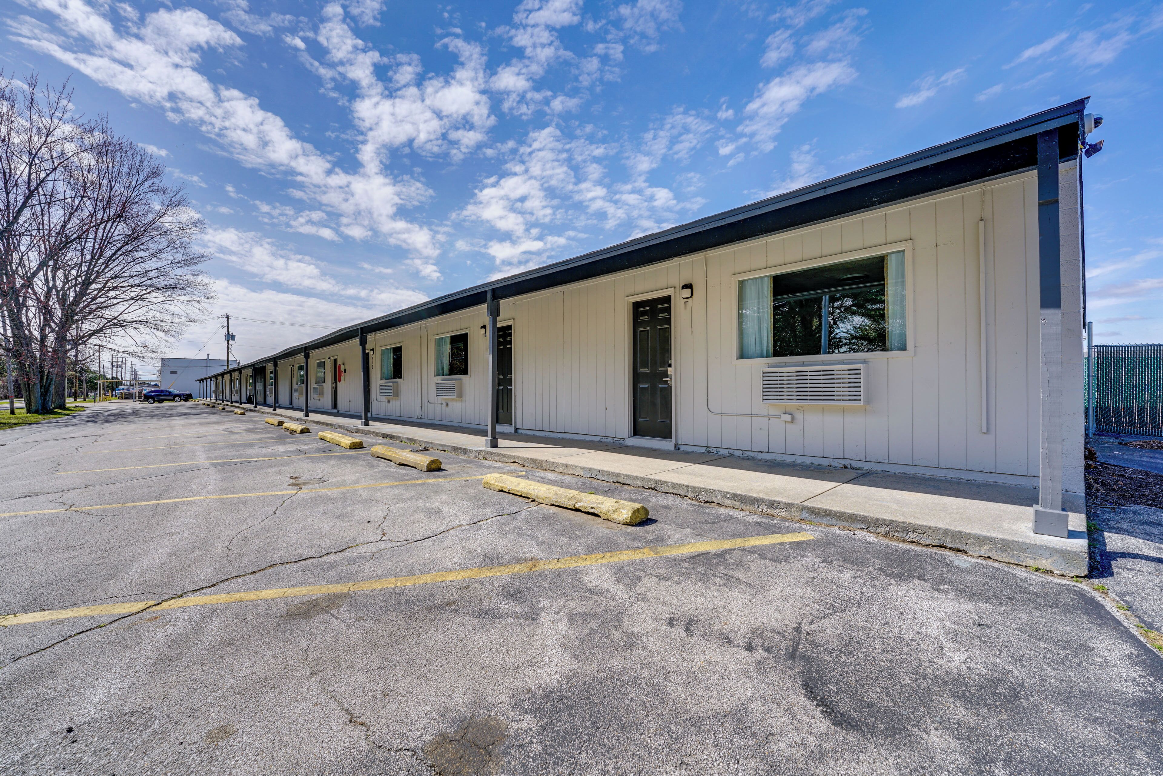 A row of single-story motel rooms with a parking lot in front.