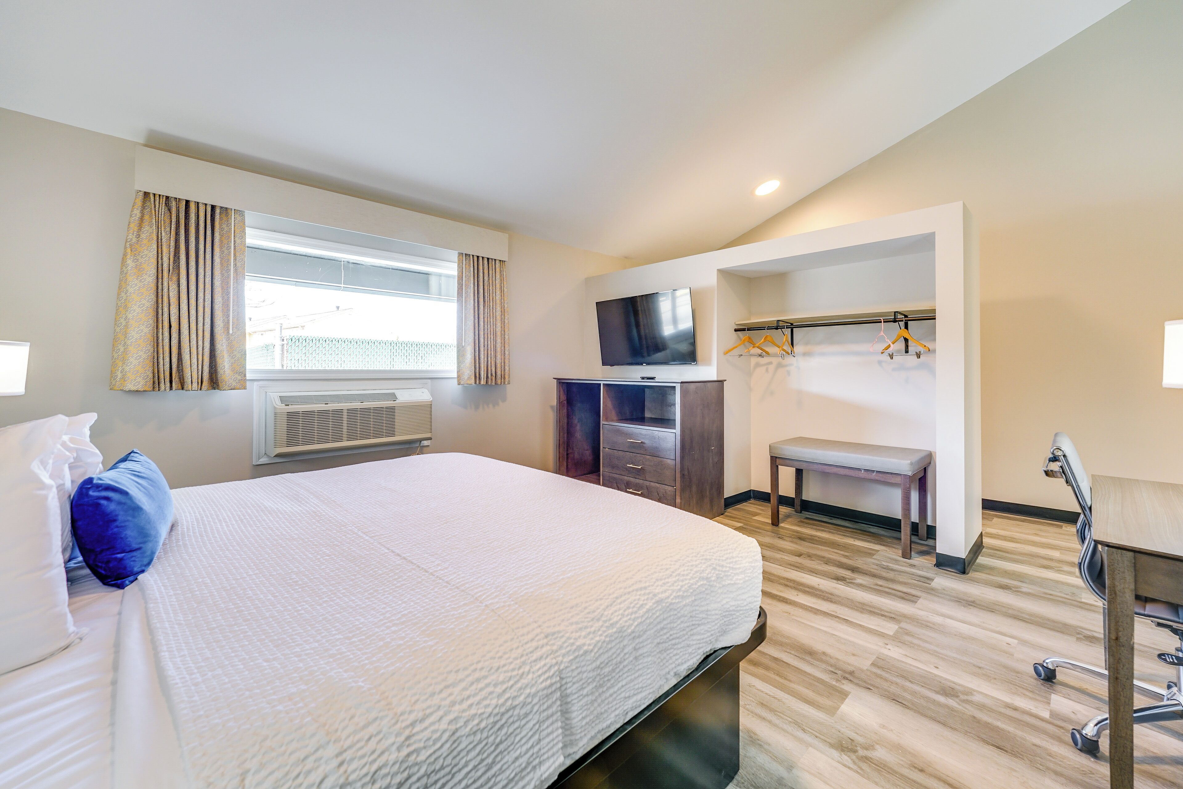 A hotel room with a large bed, a desk, a TV, and a coat rack.