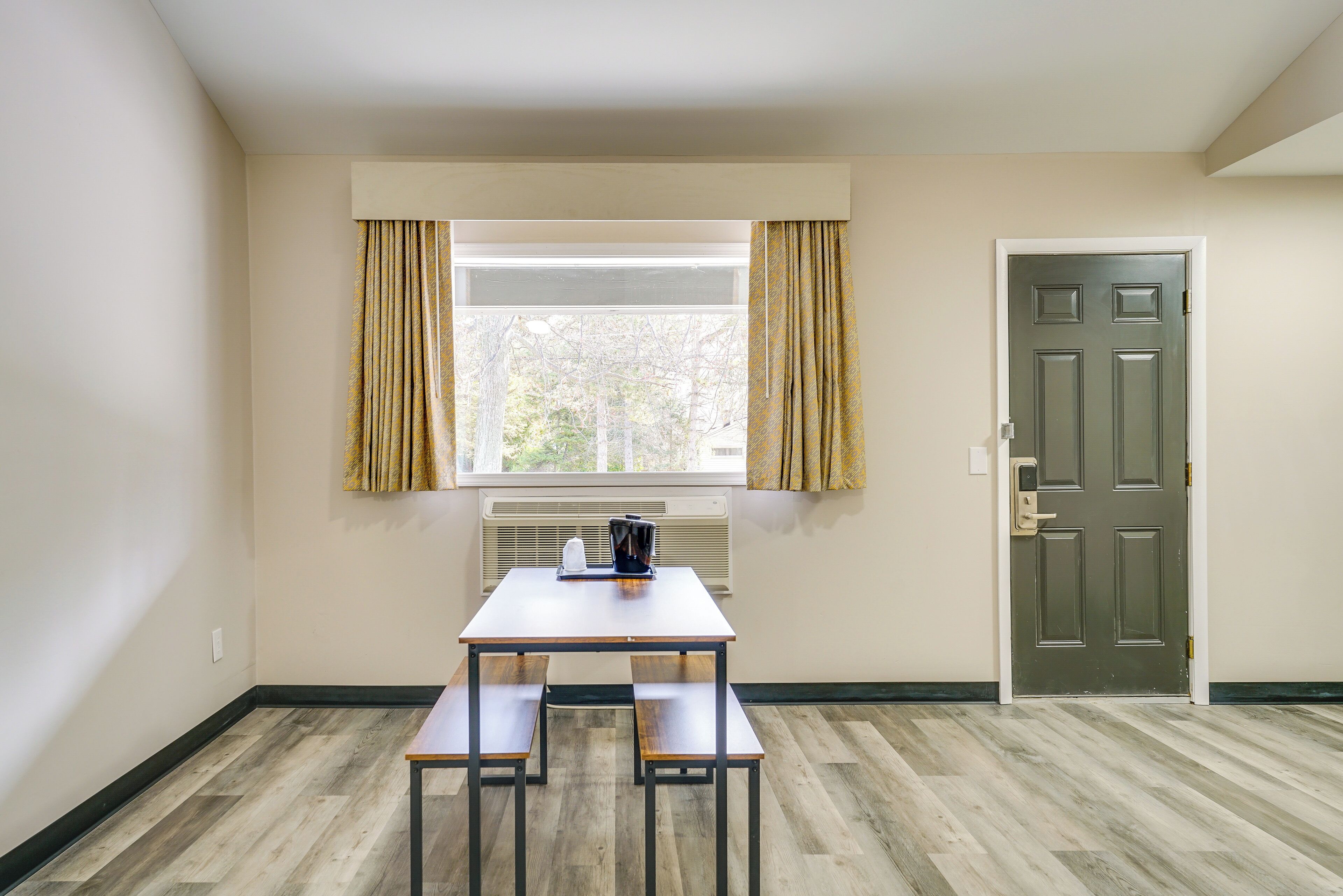 Una habitación con ventana, puerta y una mesa con bancos.