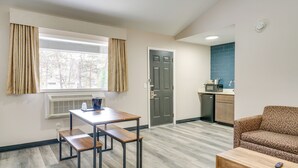 Un espacio habitable compacto con kitchenette, una zona de comedor con mesa y bancos, un sofá y una ventana con cortinas.