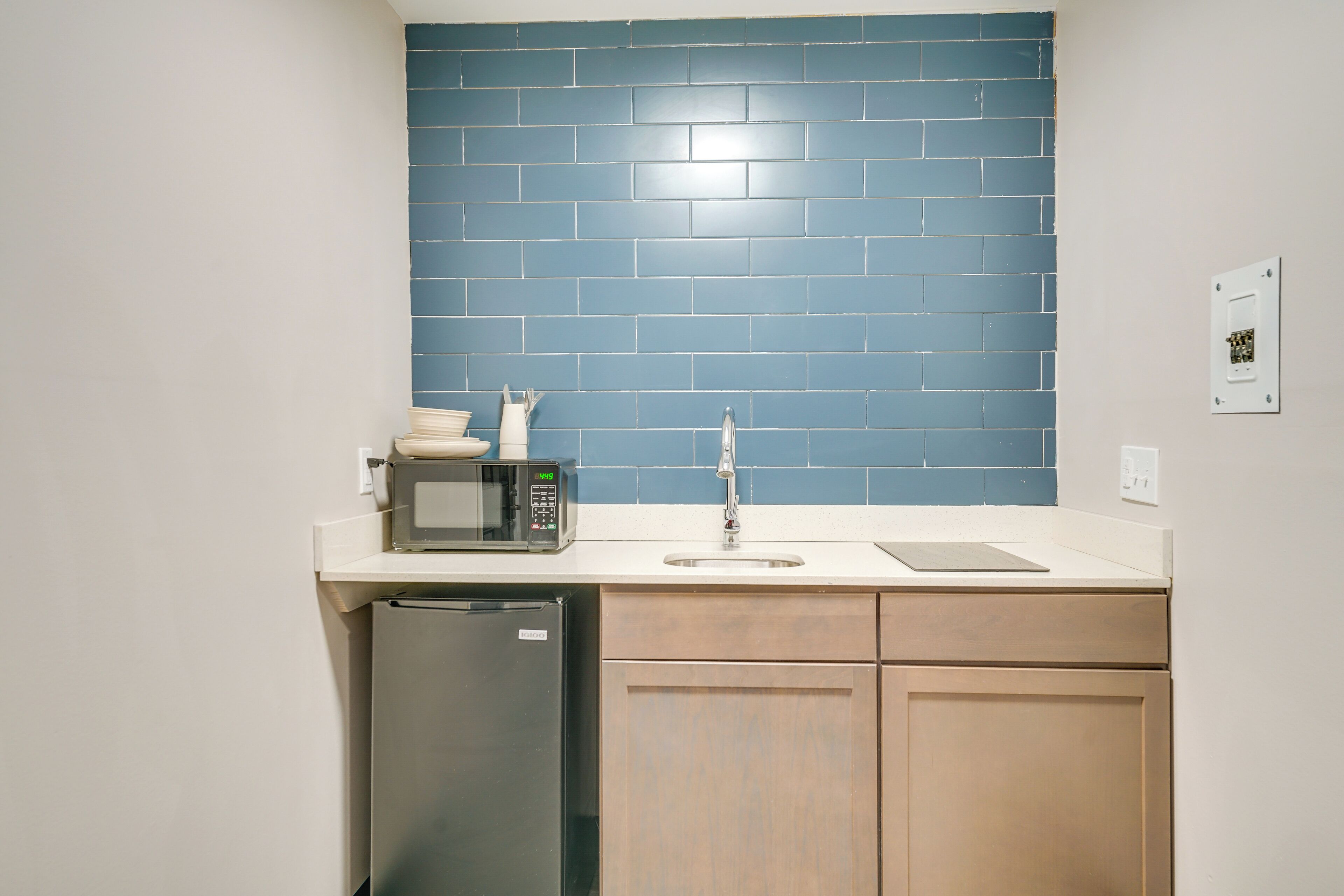 A kitchen with a blue tiled backsplash, a microwave, a sink, and wooden cabinets.