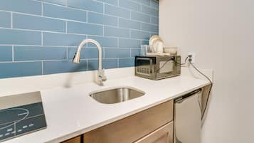 A kitchen with a stainless steel sink, a microwave, and a dish rack on the counter.