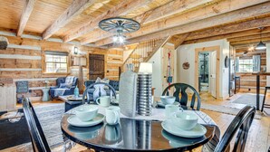 A rustic wooden interior with a dining area featuring a round table set for four, a staircase, and a living room with a sofa and chairs. - Hot Tub, Fire Pit & Creek Access: Whittier Cabin! (Whittier)