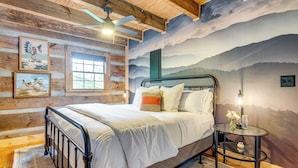 A bedroom with a bed, a round glass table, a ceiling fan, and a mural of mountains. - Hot Tub, Fire Pit & Creek Access: Whittier Cabin! (Whittier)