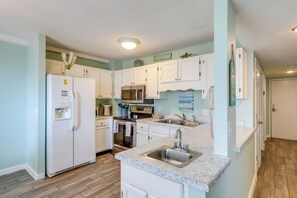 A modern kitchen with white cabinets, a stainless steel refrigerator, a microwave, and a sink.