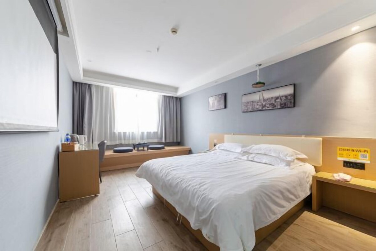 A modern hotel room with a large bed, a desk, and a window with curtains.