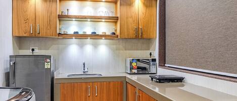 Una cocina compacta con armarios de madera, un refrigerador de acero inoxidable, un microondas y un tostador.