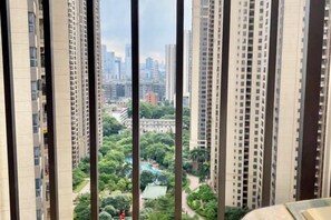 Un immeuble de grande hauteur, avec de nombreux étages, offrant une vue sur un parc arboré et un terrain de jeux, ainsi que sur le paysage urbain au loin.