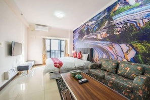 Une chambre d’hôtel avec un lit, un canapé, une télévision et un grand tableau au mur.