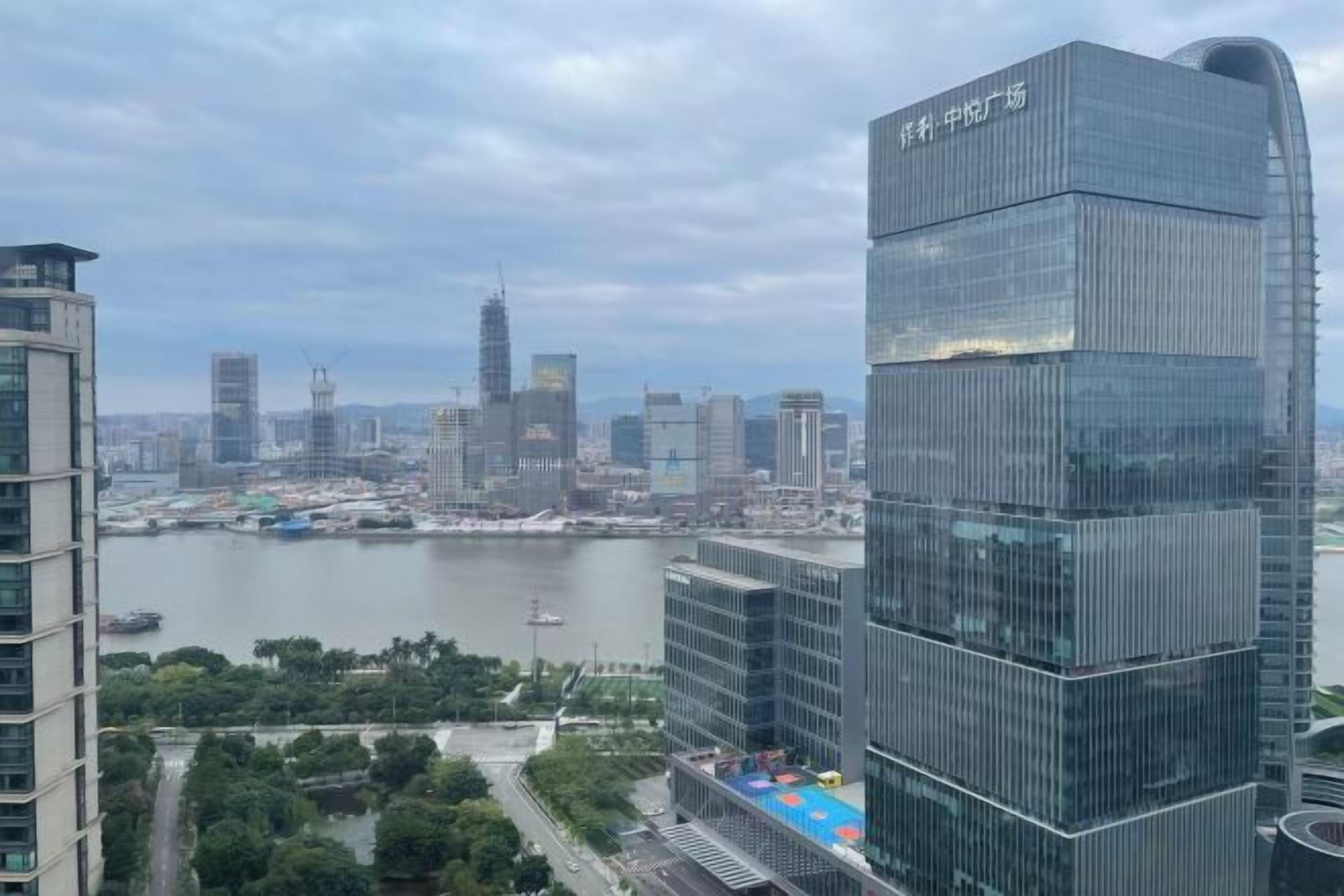 A high-rise building with a modern glass facade, situated in a cityscape with a river and other buildings in the background.