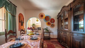 A dining room with a long table set for a meal, wooden chairs, a patterned tablecloth, and a red carpet. - Resonance Experience, Villa Retreat & Sound Healing (Sardegna)