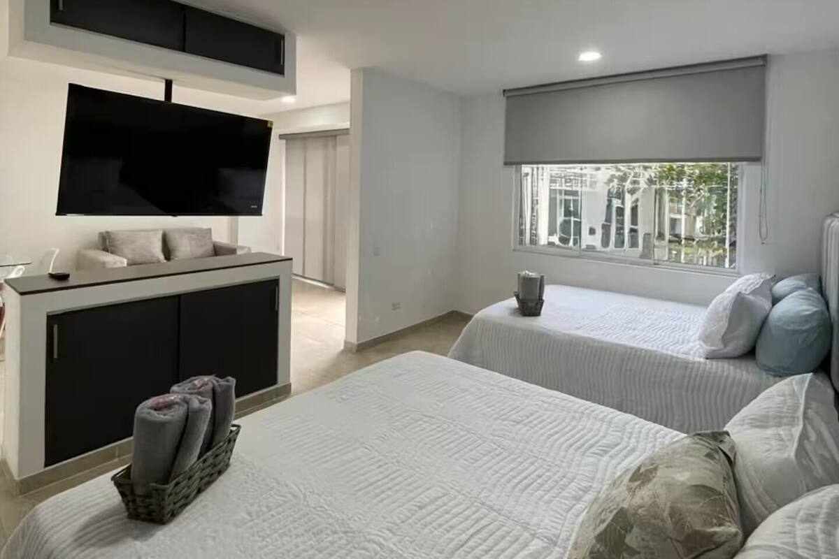 A modern bedroom with two beds, a TV, and a window with a view.