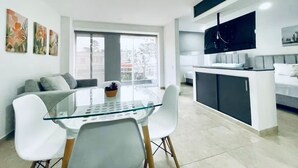 A modern living space with a glass dining table, white chairs, a sofa, a TV mounted on the wall, and a balcony with a view. - Casa Saza (Cali)