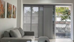A modern living room with a glass-top coffee table, a grey sofa, and a sliding glass door leading to an outdoor area. - Casa Saza (Cali)