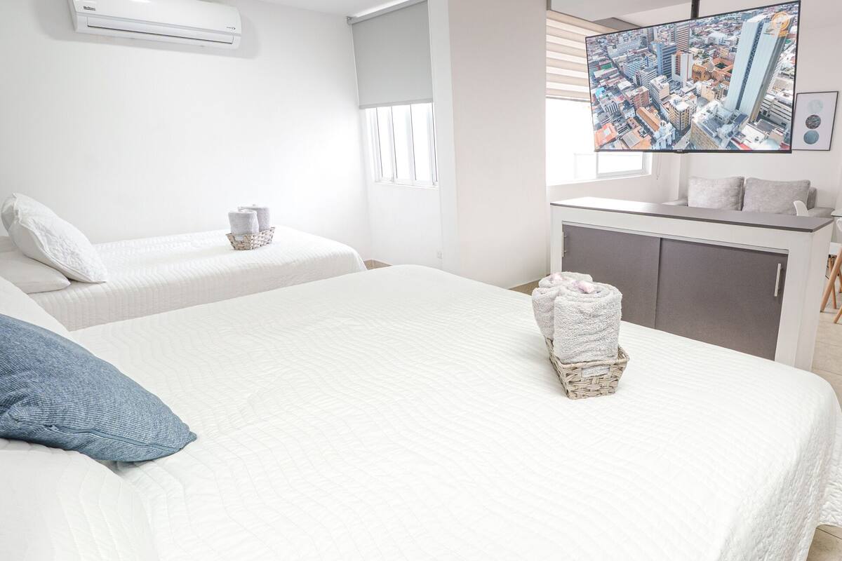A hotel room with two beds, a small desk, and a cityscape view.