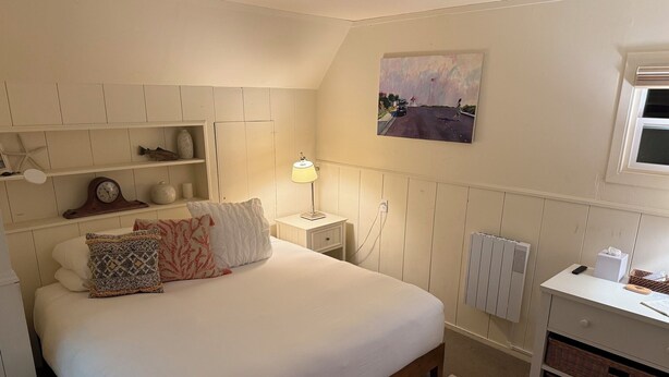 Un dormitorio con cama, mesita de noche, lámpara, decoración en la pared y un radiador.