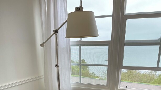 Un fauteuil gris agrémenté d’un coussin à motifs blancs et jaunes, placé près d’une fenêtre donnant sur la mer.
