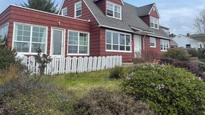 Une maison à deux étages, avec une façade rouge et des éléments décoratifs blancs, dotée de grandes fenêtres et d’une clôture blanche en bois.