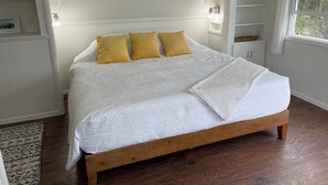 Une chambre à coucher avec un lit en bois, du linge de lit blanc et une fenêtre donnant sur des arbres.