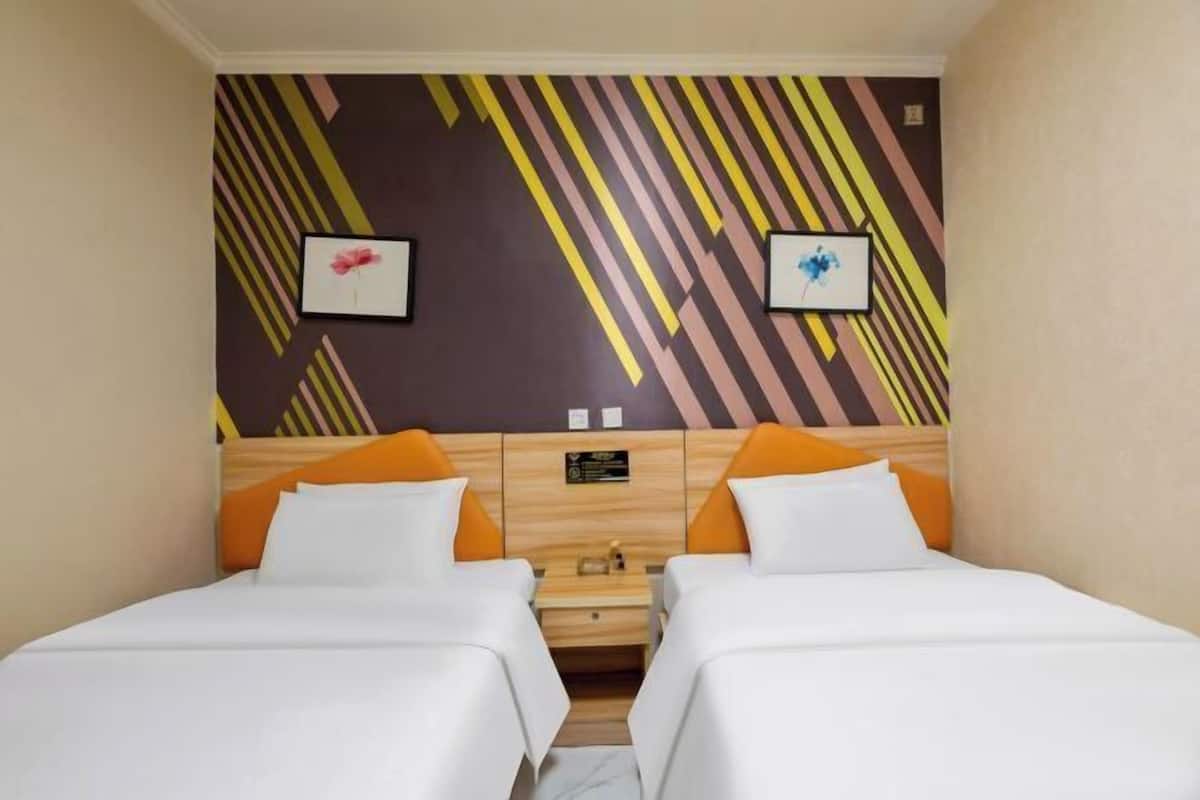 Une chambre d’hôtel avec deux lits, une tête de lit en bois et un mur orné de rayures diagonales et de tableaux encadrés.