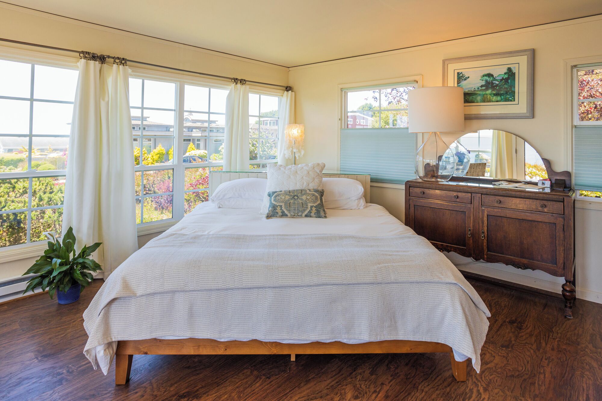 A bedroom with a large bed, a dresser, a mirror, and a window with curtains.