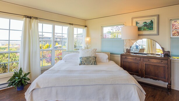 A bedroom with a large bed, a dresser, a mirror, and a window with curtains. - Large, Comfortable Room with views of both the Ocean and The Bay! (Trinidad)