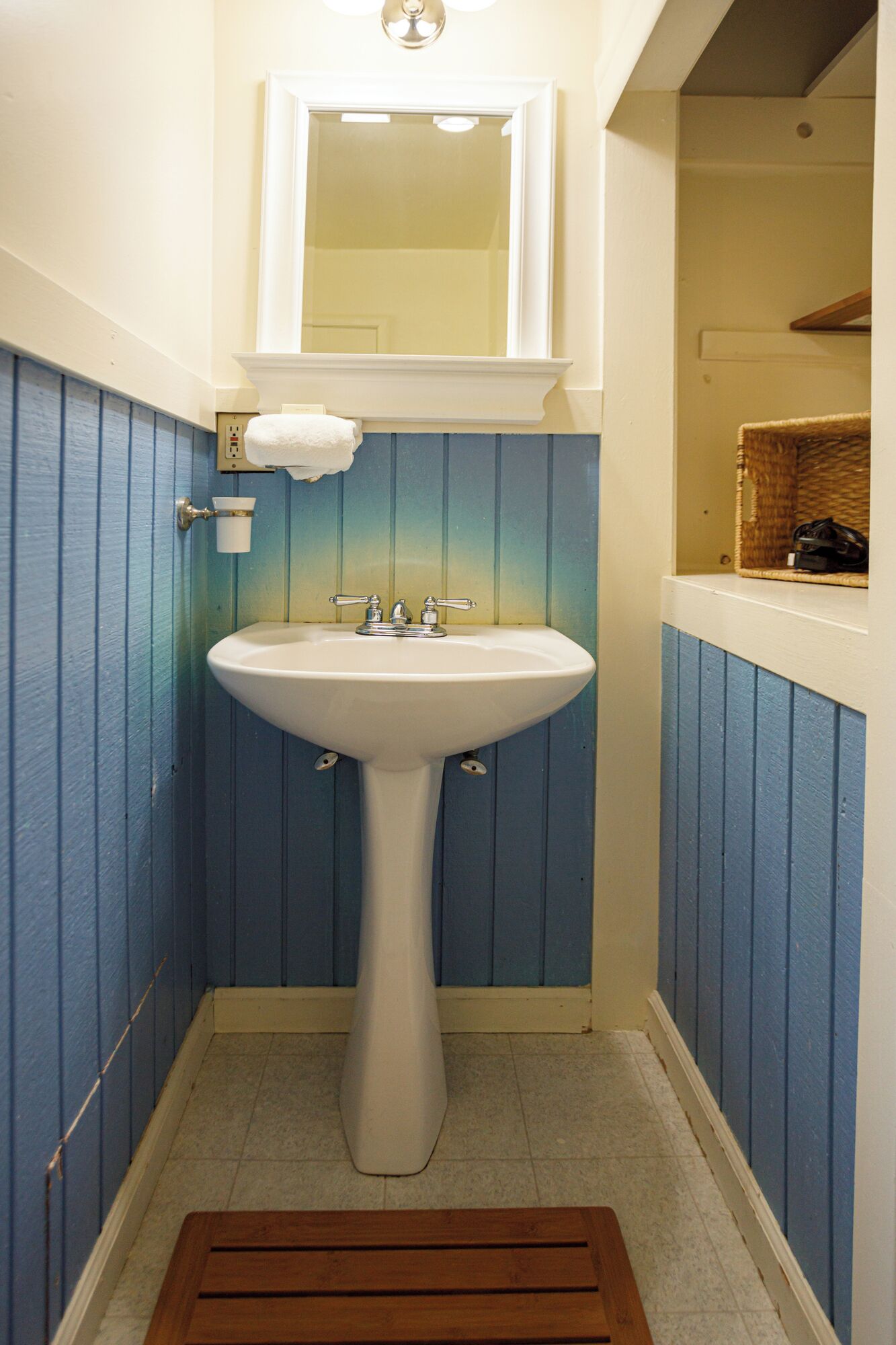 A bathroom with a white pedestal sink, a mirror above it, and a blue wall.