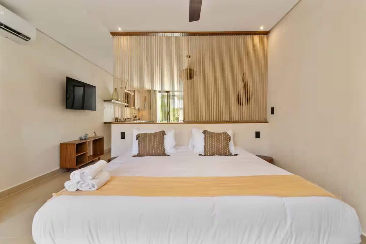 A modern hotel room with a large bed, a wooden headboard, a flat-screen TV, and a wooden side table.